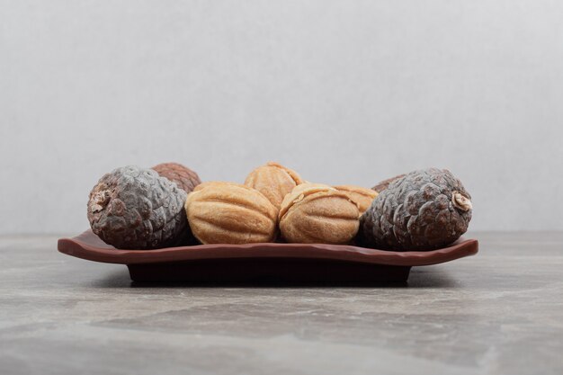 Walnussförmige Kekse und Tannenzapfen auf dunklem Teller.
