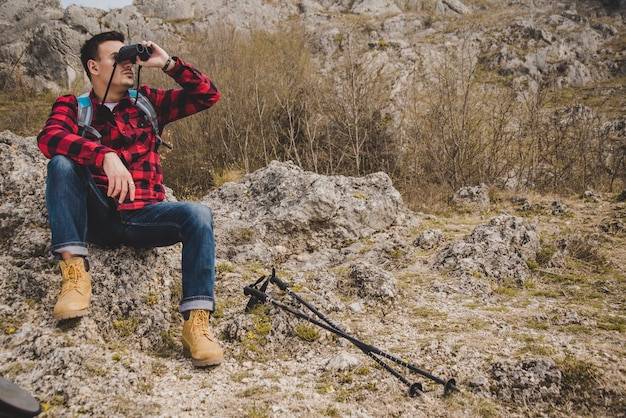 Wanderer sitzt auf einem Felsen und benutzt sein Fernglas