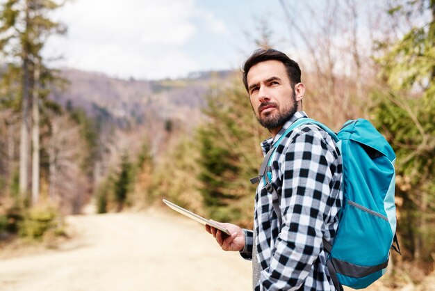 Wandernder Mann mit Rucksack und Tablet, der die Aussicht genießt