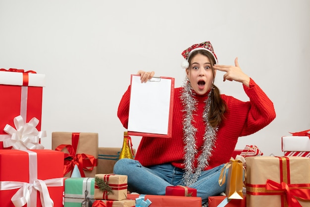 wanderte Mädchen mit Weihnachtsmütze, die Dateien hält, die feinere Waffe zu ihrer Schläfe setzen, die um Geschenke auf Weiß sitzt