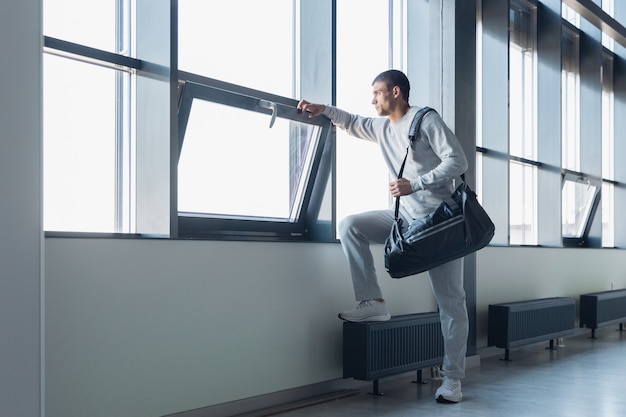 Warten auf Tor. Sportler, der in einem modernen verglasten Gebäude, Flughafen in Megapolis hinuntergeht. Vor dem Flug zum Wettkampf. Professioneller, stilvoller, selbstbewusster Athlet. Reise, Urlaub, Sportlebensstil.