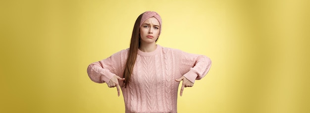 Kostenloses Foto warum ich meine güte. düstere aufregung, die sich beschwert, süßes, glamouröses, junges europäisches mädchen im lässigen pullover, stirnband, das die stirn runzelt, jammernd grimassen verzieht, unzufrieden nach unten zeigt, unglücklich sieht, wie viel arbeit über die gelbe wand geht