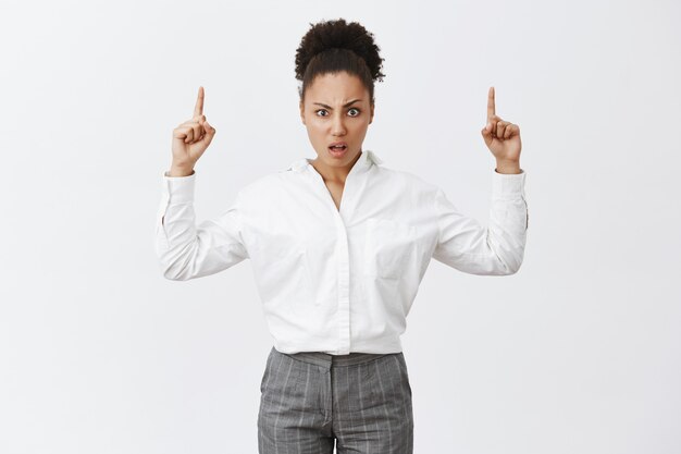Was zum Teufel. Porträt einer missfallenen verwirrten Afroamerikanerin mit Brötchenfrisur in weißem Hemd und Hose, die fragend und enttäuscht starrte, während sie mit erhobenen Händen nach oben zeigte