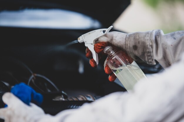 Waschanlagearbeitskraft, die eine weiße Uniform steht einen Schwamm trägt, um das Auto in der Waschanlagemitte, Konzept für Autopflegeindustrie zu säubern.