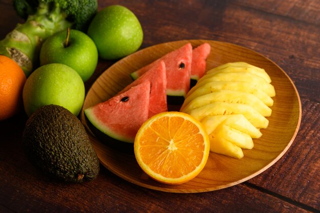 Wassermelone, Ananas, Orangen, in Stücke geschnitten mit Avocado, Brokkoli und Äpfeln auf Holztisch. Draufsicht.