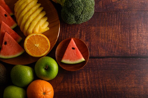 Wassermelone, Ananas, Orangen, in Stücke geschnitten mit Avocado, Brokkoli und Äpfeln auf Holztisch. Draufsicht.