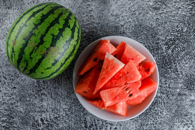 Wassermelone mit Scheiben auf grauem Grunge-Tisch