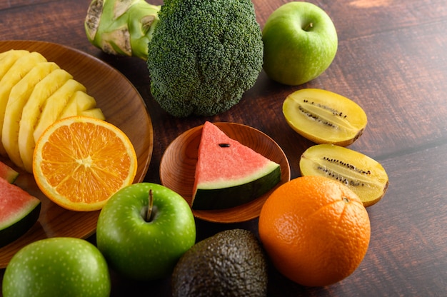 Wassermelone, Orange, Ananas, Kiwi in Scheiben geschnitten mit Äpfeln und Brokkoli auf einem Holzteller und Holztisch.