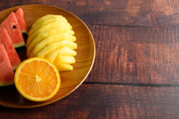 Wassermelone, Orange und Ananas auf einem Holzteller in Stücke geschnitten