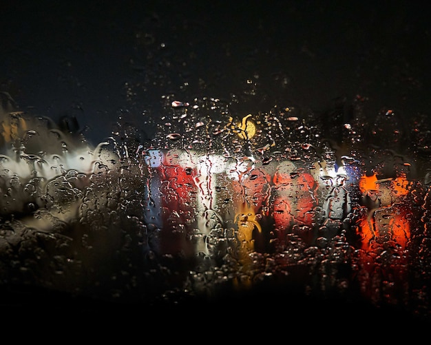 Wassertropfen am Fenster verwischen die Lichter draußen mit einem Schwarz