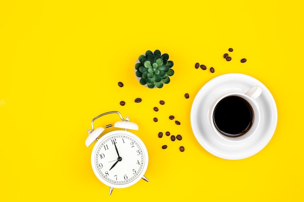 Wecker Tasse Kaffee und Kaffeebohnen auf gelbem Hintergrund flach gelegt