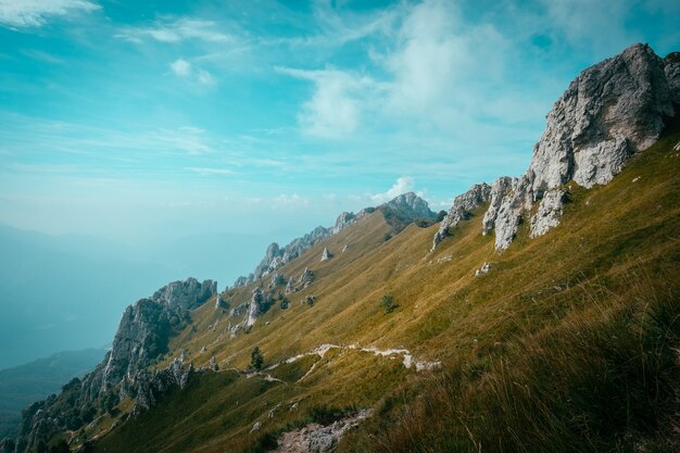 Weg auf einem Hügel in der Mitte eines Grasfeldes mit felsigen Klippen mit einem blauen Himmel