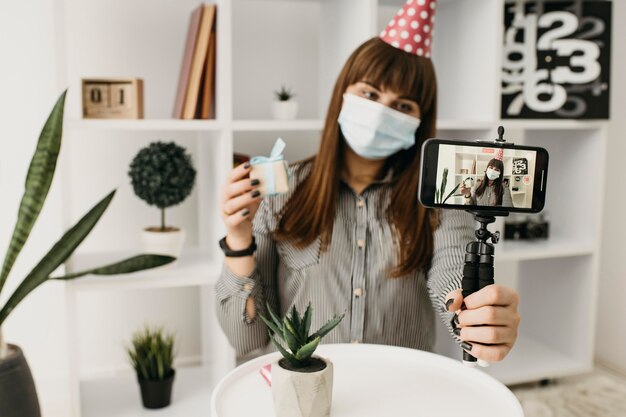 Weibliche Bloggerin mit medizinischer Maske, die Geburtstag mit Smartphone strömt