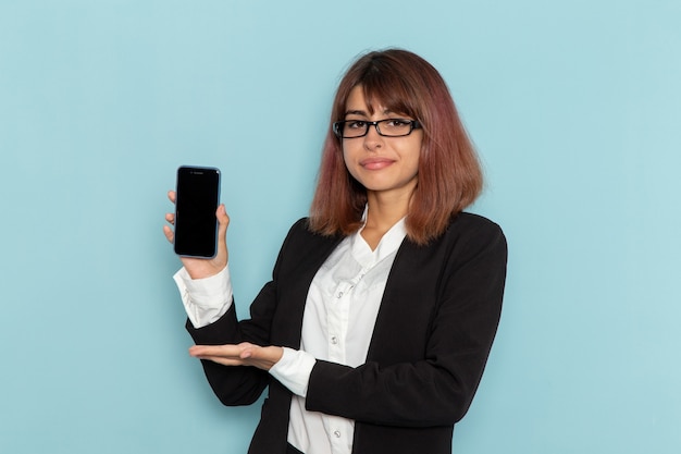 Weibliche Büroangestellte der Vorderansicht im strengen Anzug, der ihr Smartphone auf blauer Oberfläche hält