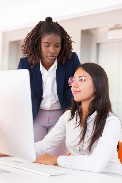 Weibliche Bürokollegen, die Arbeitsfragen am Desktop besprechen