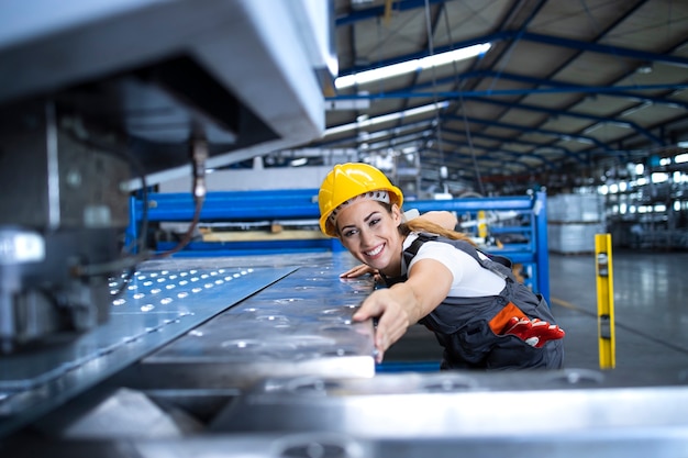 Weibliche Fabrikarbeiterin in Schutzuniform und Helm, die Industriemaschine an der Produktionslinie betreibt