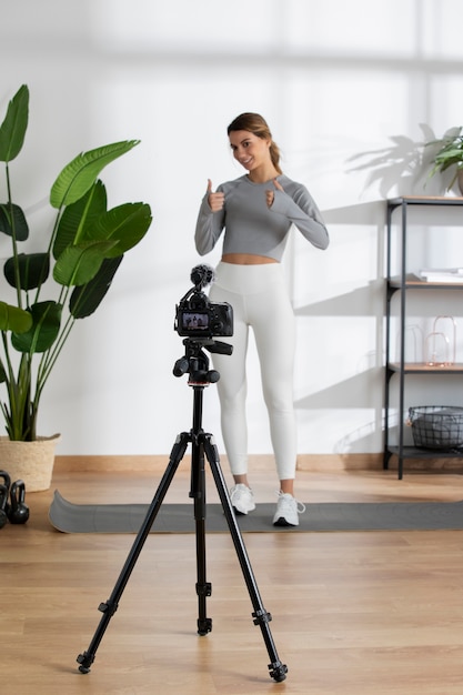 Weibliche Fitnesstrainerin unterrichtet einen Online-Kurs von zu Hause aus mit einer Kamera auf einem Stativ