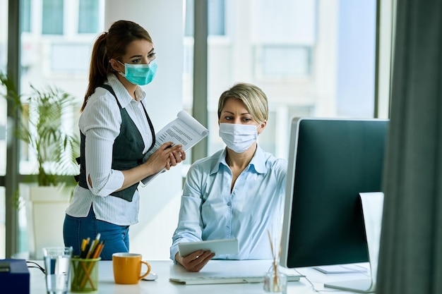 Weibliche Geschäftskollegen mit Gesichtsmasken, die im Büro arbeiten und eine E-Mail auf einem Computer lesen