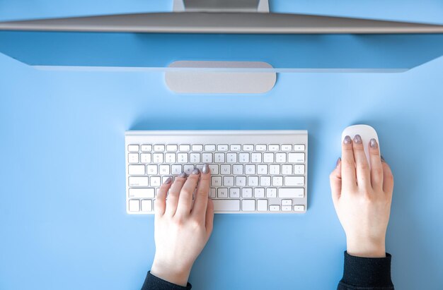 Weibliche Hände der Draufsicht arbeiten am blauen Hintergrund des Computers