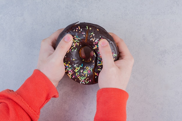 Weibliche Hände, die Donut auf Steinoberfläche halten.