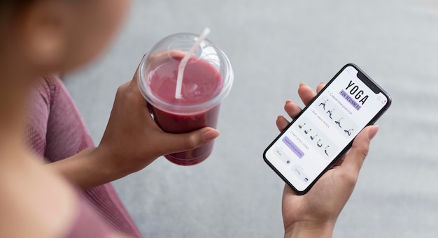 Weibliche hände, die einen fruchtsaft und ein smartphone mit yoga-app halten