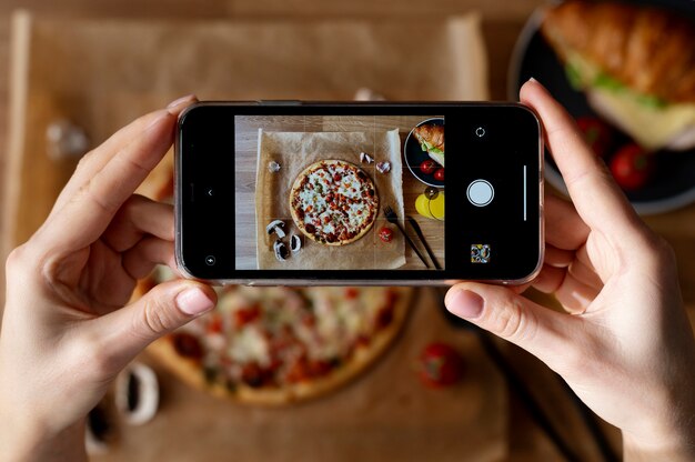 Weibliche Hände, die Foto von geschnittener Pizza machen