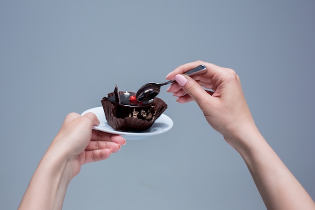 Weibliche Hände, die Kuchen mit Löffel auf grau halten