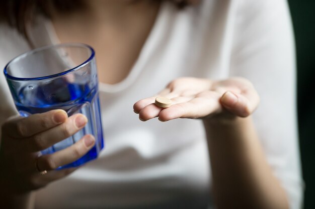 Weibliche Hände, die Pille und Glas Wasser, Nahaufnahmeansicht halten