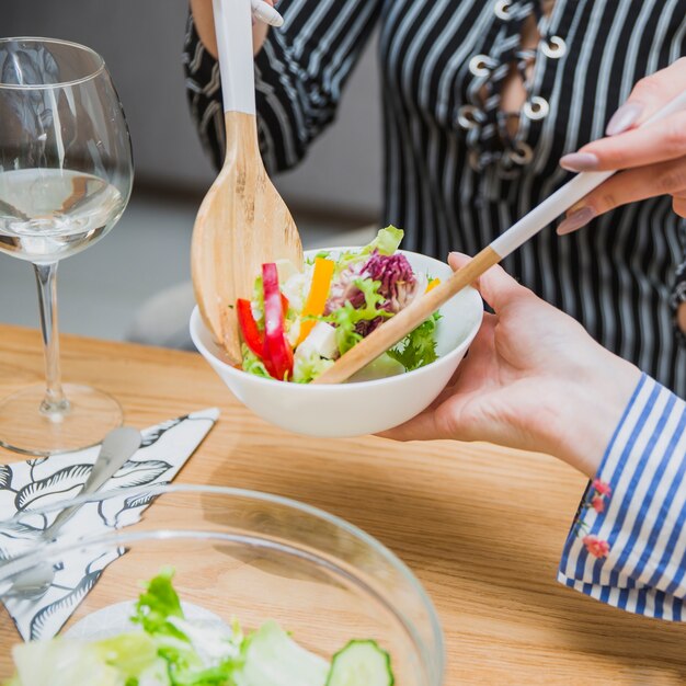 Weibliche Hände, die Salat mit hölzernen Löffeln nehmen