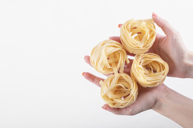 Weibliche Hände, die Tagliatelle-Nester auf Weiß halten.