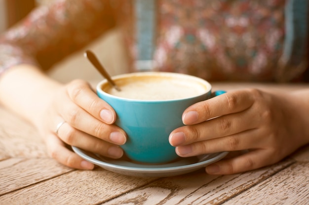 Weibliche Hände, die Tasse Kaffee mit Schaum auf Tabelle halten