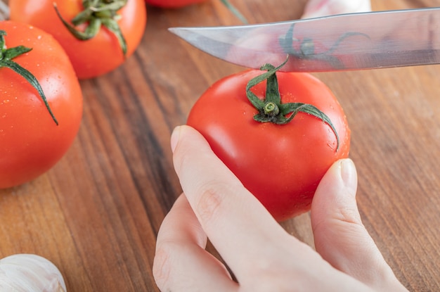 Weibliche Hände, die Tomaten mit Messer schneiden.