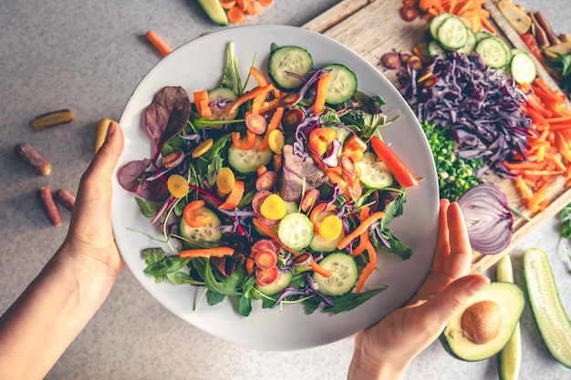 Kostenloses Foto weibliche hände halten eine schüssel veganen salats mit frischem gemüse oben