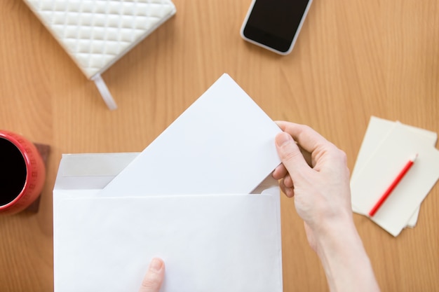 Weibliche Hände halten einen Umschlag mit einem Blatt über dem Büro de