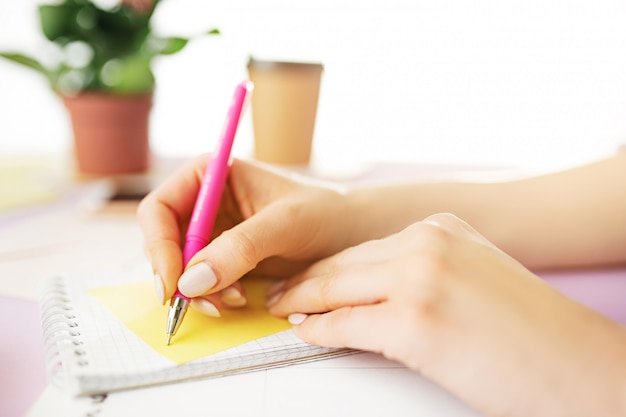 weibliche Hände halten Stift. Telefon auf trendigen rosa Schreibtisch.