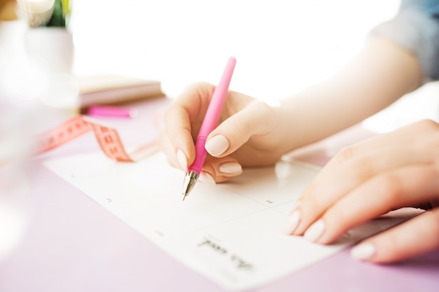 weibliche Hände halten Stift. trendiger rosa Schreibtisch.