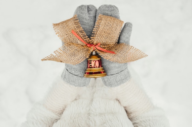 Weibliche Hände in gestrickten Handschuhen mit einer dekorativen Glocke für Weihnachtsdekoration