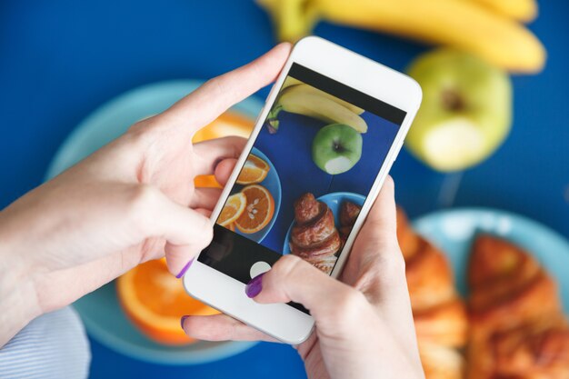 Weibliche Hände machen Foto mit Telefon am Essen