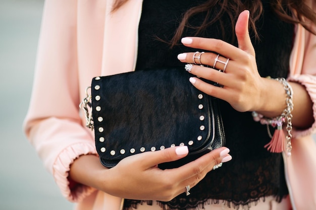Weibliche Hände mit schönem Nagellack und Ringen, die kleine schwarze Tasche halten.