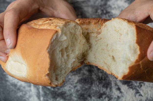 Weibliche Hände Nahaufnahme, die frisches Baguettebrot bricht.