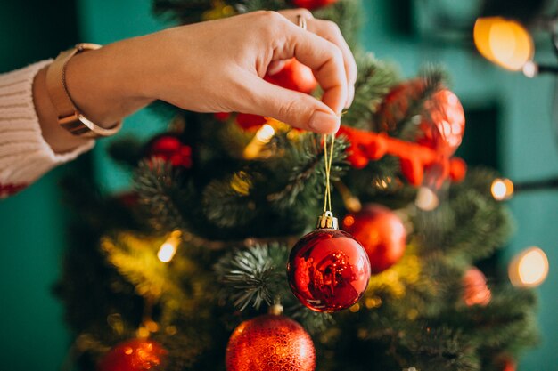 Weibliche Hände schließen oben und verzieren Weihnachtsbaum mit roten Bällen