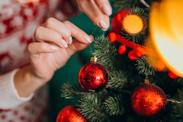 Weibliche Hände schließen oben und verzieren Weihnachtsbaum mit roten Bällen