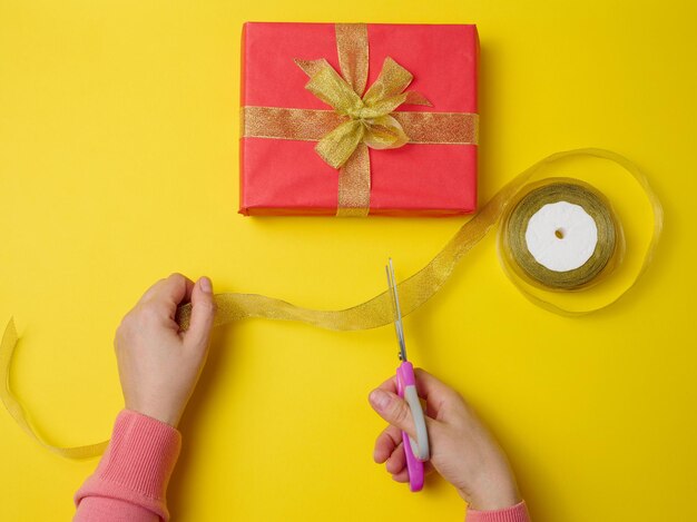 Weibliche hände schneiden mit einer schere ein seidenband neben geschenkboxen. gelber hintergrund, ansicht von oben