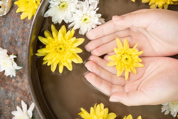 Weibliche Hände und Schüssel des Spa-Wassers mit Blumen, Nahaufnahme. Hände Spa.