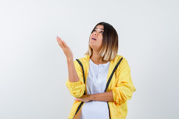 Weibliche Hand anheben, während in T-Shirt, Jacke und erstaunt, Vorderansicht nach oben schauend.