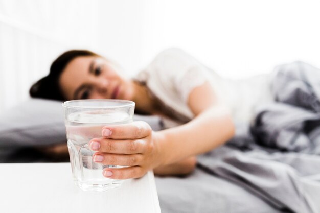 Weibliche Hand der Nahaufnahme, die für Glas Wasser erreicht