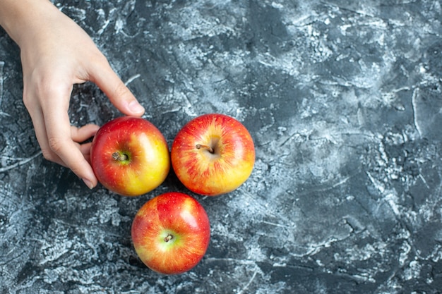 Weibliche Hand der reifen Äpfel der Draufsicht auf grauem Hintergrund mit Kopienplatz