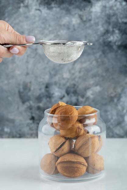 Weibliche Hand, die ein Zuckerpulver auf walnussförmige Kekse streut.