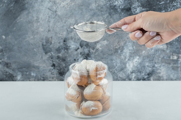 Weibliche Hand, die ein Zuckerpulver auf walnussförmige Kekse streut.