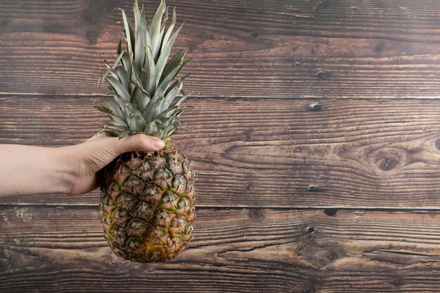 Weibliche Hand, die einzelne frische Ananas auf hölzernem Hintergrund hält